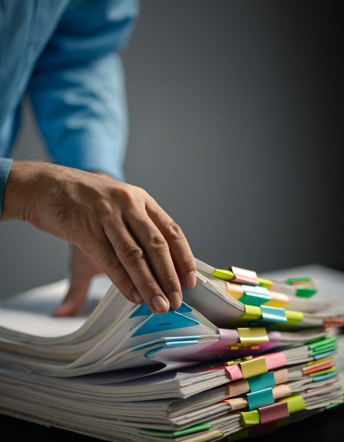 Person with stacks of company financial report papers in office, company employee picking up papers on table to use for performance summary and filing. Document management concept.